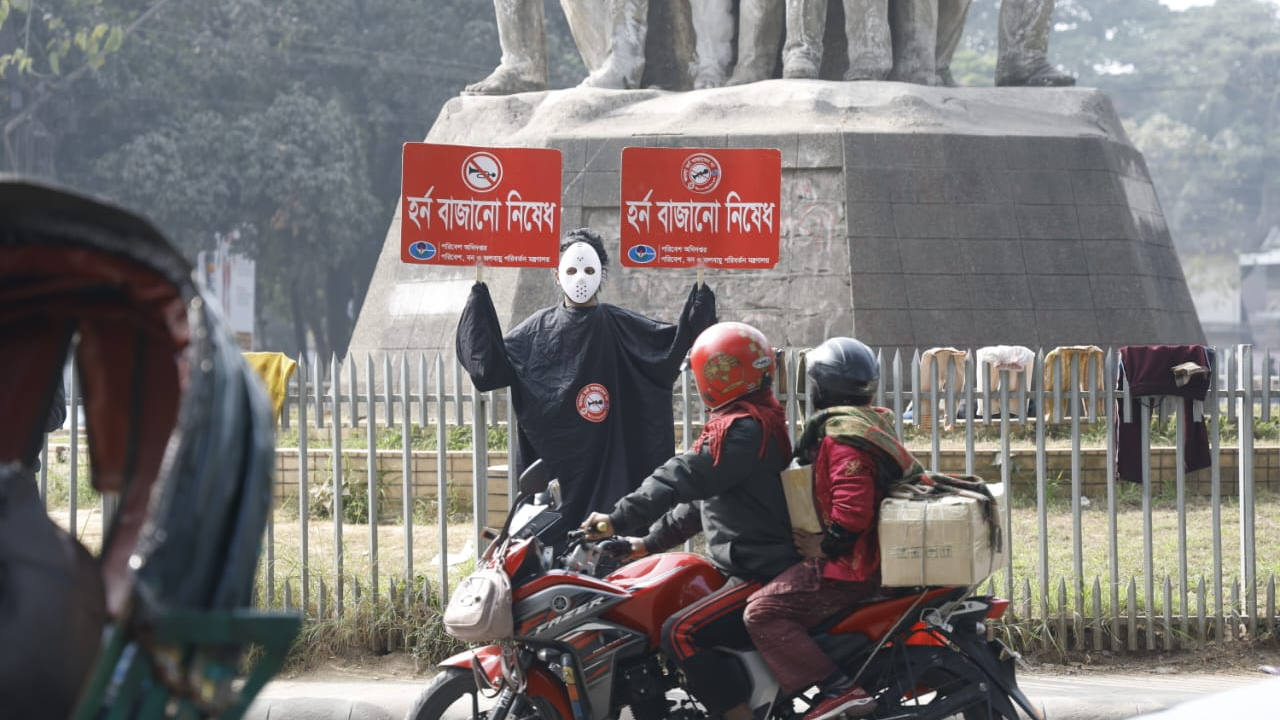 শব্দদূষণ রোধে ঢাকা বিশ্ববিদ্যালয়ের রাজু ভাস্কর্যের সামনে ব্যতিক্রমী পোশাকে প্ল্যাকার্ড প্রদর্শন।