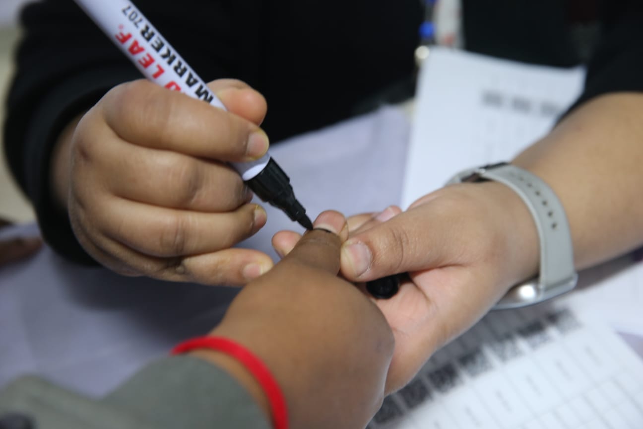 ভোটারের আঙুলে কালি দিয়ে দিচ্ছেন ভোটের কাজে নিয়োজিত কর্মকর্তা।