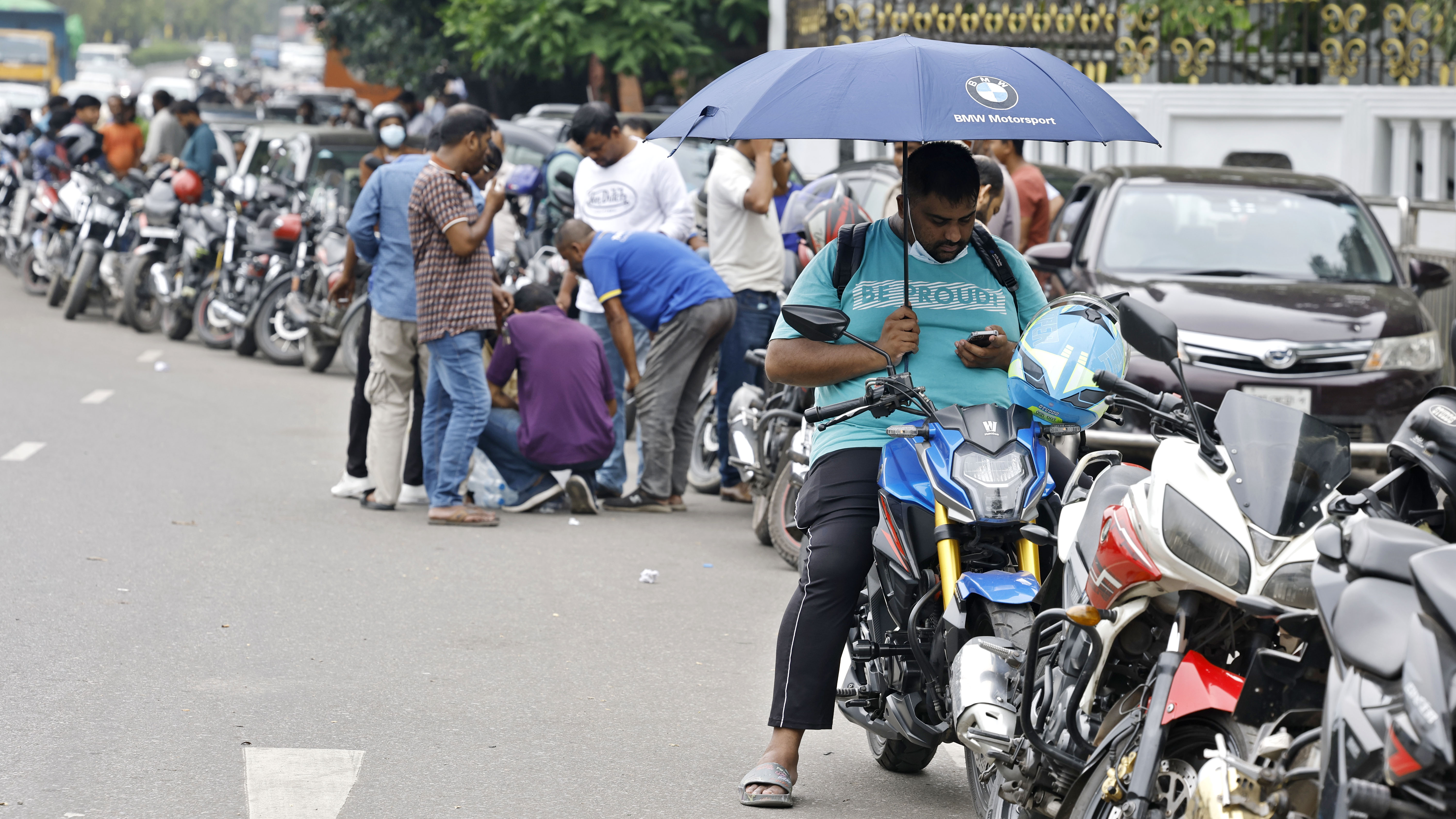 প্রচন্ড রোদ থেকে বাঁচতে তেলের জন্য ছাতা নিয়ে লাইনে অপেক্ষা করছেন একজন